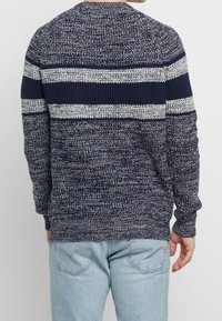 Suéter de punto en azul marino y blanco con rayas horizontales. Presenta una tela texturizada y un cuello redondo. Combinado con jeans de color azul claro.