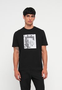 Camiseta de algodón negra con un gráfico frontal de un oso polar rugiente en blanco y negro, enmarcado por un borde rectangular con patrones de hojas.