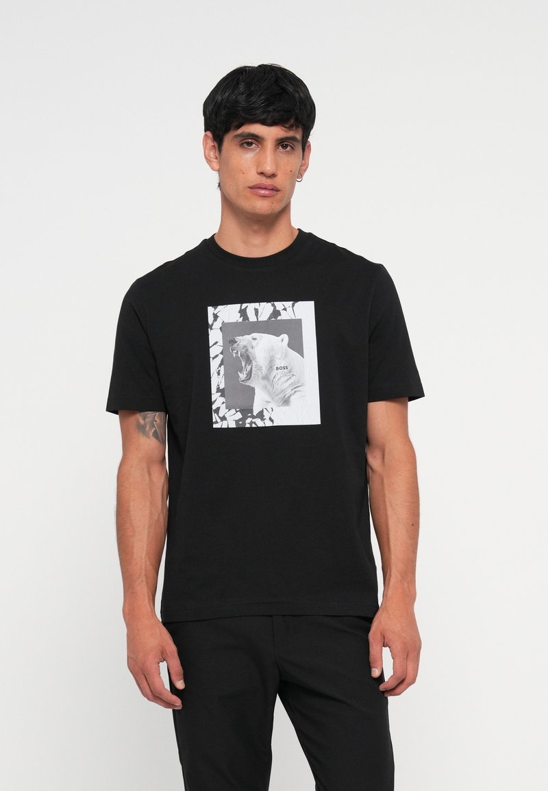 Camiseta de algodón negra con un gráfico frontal de un oso polar rugiente en blanco y negro, enmarcado por un borde rectangular con patrones de hojas.