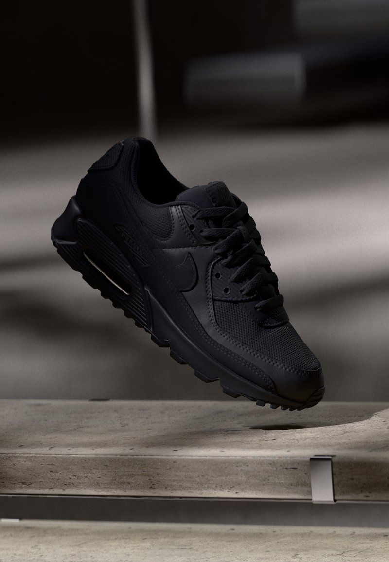 Zapatilla Nike Air Max 90 negra que presenta un upper de malla texturizada, suela de goma y un distintivo acolchado Air visible en el talón.