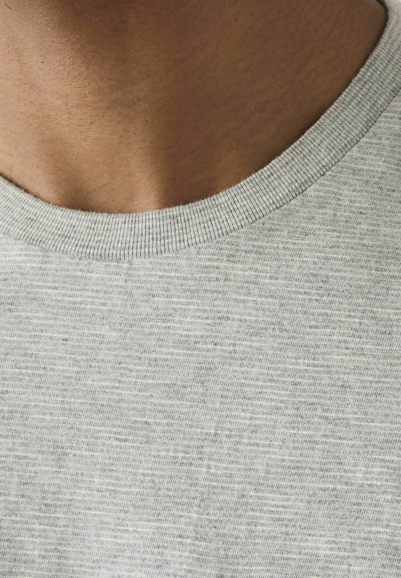 Gros plan sur le cou et le haut de la poitrine d'une personne portant un t-shirt gris clair à col rond.