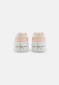 Roosa ja valge Calvin Klein Jeansi tenniser pair vaadatuna tagant, paksude valgete talladega, millel on logo, valge tausta ees.