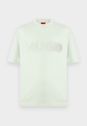 T-shirt blanc à manches courtes col rond avec un grand texte embossé "HUGO" sur la poitrine et une étiquette rouge à l'intérieur du col.