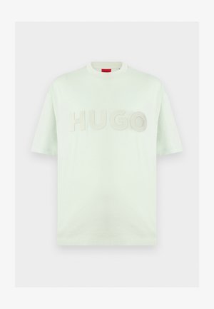 T-shirt blanc à manches courtes col rond avec un grand texte embossé "HUGO" sur la poitrine et une étiquette rouge à l'intérieur du col.