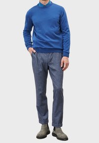 Maglione blu a maglia con colletto rotondo, abbinato a pantaloni grigi a trama e stivaletti grigi alla caviglia, che mostrano un fit rilassato.