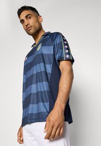 Polo bleu marine avec des rayures horizontales dans des nuances de bleu, doté d'un col, de manches courtes et d'un logo sur le devant et les manches.