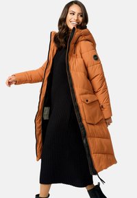 Long orange puffer coat with a hood and side pockets, featuring a black zipper and trim. Worn over a black ribbed knit dress.