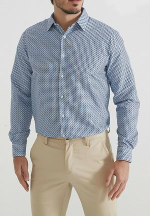 Chemise bleue à boutons avec un motif géométrique de petites formes bleu marine sur un fond bleu clair, manches longues et col classique.