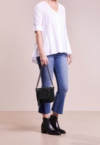 Camicia bianca con maniche arrotolate, jeans blu a vita alta e cropped, stivali neri con borchie alla caviglia e una piccola borsa nera a tracolla con catena.