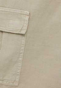 Tissu beige avec une texture lisse et une poche plaquée soigneusement cousue. Le design présente une forme simple et fonctionnelle.