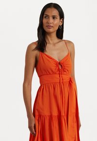 Vestido de algodão laranja com alças finas, corpete franzido, detalhe de laço ajustável e uma saia fluida com camadas de babados.