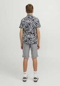 Camicetta a maniche corte blu navy con motivi di foglie bianche, abbinata a pantaloni corti grigi arrotolati. L'outfit presenta una vestibilità rilassata e calzature casual.