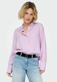 Chemise rose pâle à boutons avec des rayures verticales bleues, manches longues, coupe décontractée, associée à un jean taille haute bleu clair et une ceinture noire.