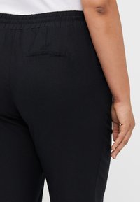 Pantaloni neri con elastico in vita, dal tessuto liscio, dotati di una tasca sul retro e dal design aderente, adatti per un look casual.