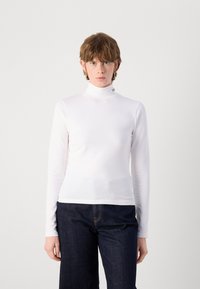 White long-sleeve turtleneck shirt made of smooth fabric, featuring a slim fit and subtle branding detail near the collar. Dark jeans below.