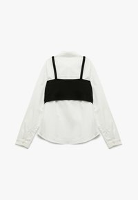Camicia bianca a maniche lunghe con top corto nero sovrapposto, dotata di colletto classico e polsini abbottonati. Tessuto morbido con colori a contrasto.