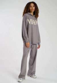 Graues Loungewear-Set mit einem langen Hoodie, auf dem "MIAMI" in cremefarbenen Buchstaben steht, und dazu passenden ausladenden Hosen, gefertigt aus weichem, strukturiertem Stoff.