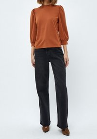 Hnědý přiléhavý top s nabíranými rukávy, zkombinovaný s černými kalhotami s vysokým pasem a širokými nohavicemi. Hnědé podpatkové boty dotvářejí celý outfit.