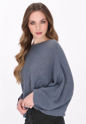 Losse trui van zacht, gestructureerd blauw garen met een wijde halslijn en lange, volumineuze mouwen. Gecombineerd met zwarte jeans.