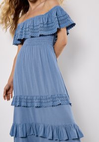Elegantes, schulterfreies blaues Kleid mit gestuftem Rüschendesign, ausgestattet mit Spitzenakzenten und einem gerüschten Oberteil, aus leichtem Stoff mit weicher Textur.