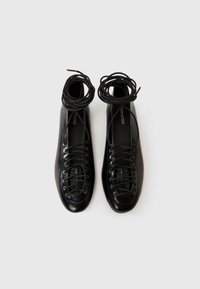 Fekete bőr cipő kerek orral, fűzős kialakítással és vékony cipőfűzőkkel. Simább textúra és minimalista stílus.