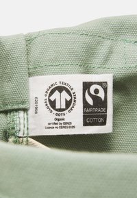Groen katoenen label met GOTS- en Fairtrade-logo's, met tekst die organische certificering en licentiegegevens aangeeft.