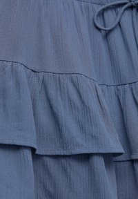 Blå, lättvikts tyg med en texturerad yta har lager av volanger. Designen är lös passform med en knuten midjedetalj.