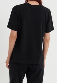 Camiseta de algodón negra con mangas cortas y cuello redondo. Presenta un corte relajado y un dobladillo recto; diseño simple sin patrones adicionales.