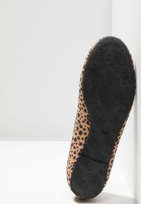 Semelle d'une chaussure plate à imprimé léopard montrant un fond en caoutchouc noir avec des motifs paisley et cœur, positionnée sur une surface blanche.