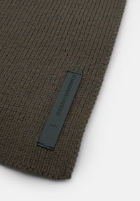 Brun strikket halsedisse med ribbet struktur. Har et sort mærke med "ALTERNATIVE CULTURE" præget. Enkel og funktionel design.