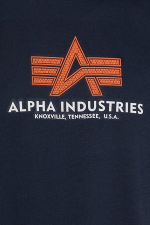 Marinblå T-shirt med en orange grafisk logotyp, med en stiliserad "A"-design och texten "Alpha Industries" nedanför i vitt.