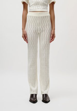 Knit pants in cream with a wavy pattern, featuring a fitted waistband and a semi-sheer texture, paired with brown heeled boots.
