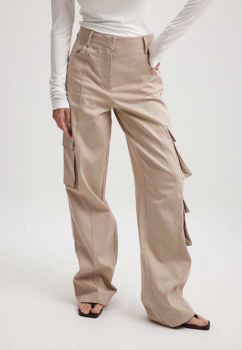 Beige cargobroek met een hoge taille, wijde benen, zij- en voorkezen met kleppen. De stof heeft een gladde textuur.
