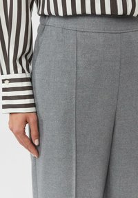 Szare dopasowane spodnie wykonane z teksturowanej tkaniny, z bocznymi kieszeniami i gładkim paskiem, zestawione z pasiastą koszulą z długim rękawem.