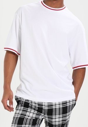 Biała koszulka z krótkim rękawem, z czerwonym mającym prążki dekoltem. W zestawie z czarno-białymi spodniami w kratę.