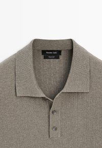 Polo en coton côtelé marron clair avec col et deux boutons, étiquette indiquant "Massimo Dutti" et "100 % coton, fabriqué en Chine."