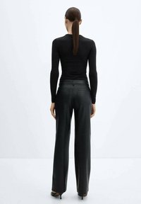 Maglietta nera a maniche lunghe e pantaloni neri a vita alta realizzati in materiale testurizzato, con una silhouette aderente e gambe larghe. Tacchi alti visibili.