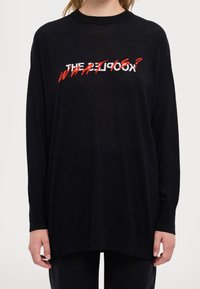 Czarny sweter z długim rękawem z czerwoną i białą grafiką tekstową "THE KOOKS?" na piersi, o luźnym kroju i ściągaczu na dole.