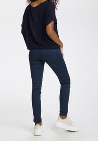 Top blu navy morbido con maniche corte, abbinato a jeans skinny in denim scuro. Le scarpe presentano suole chunky di colore chiaro.