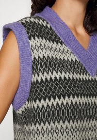 Gestrickter ärmelloser Pullover mit lila V-Ausschnitt und gemusterter Oberfläche in Schwarz und Creme, mit Zickzackmuster.