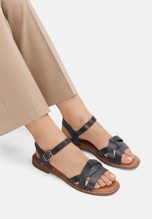 Sandały na paskach wykonane z ciemnoniebieskiej skóry, z krzyżującym się wzorem i paskami wokół kostki. Brązowa podeszwa z dekoracyjnym przeszyciem.