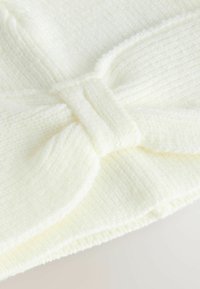Knitted headband in soft, cream-colored fabric; features a bow detail at the front with a ribbed texture and smooth finish.