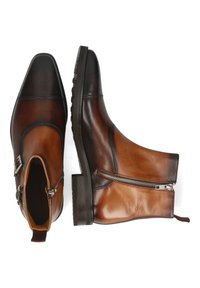 Botas de cuero marrón hasta el tobillo con punta afilada, puntera negra en contraste, cierre de cremallera y detalles de hardware metálico. Suela de goma texturizada.