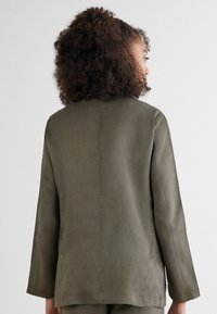 Olivgrön linneblazer med en avslappnad passform, långa ärmar och rak nederkant. Har en enkel, ren design med minimala sömnadsdetaljer.