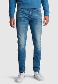 Světle modré džíny s úzkým střihem, s vyblednutím na stehnech, pěti kapsami a zipovým zapínáním. V kombinaci s bílými teniskami.