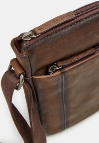 Brown leather bag with adjustable fabric strap, featuring a zippered compartment and a small zipper pocket on the front for additional storage.