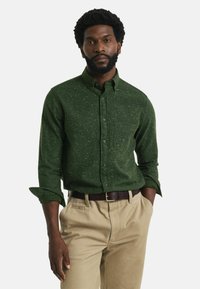 Groen gespikkelde overhemdd met lange mouwen, borstzak en een brede kraag, gecombineerd met lichtbeige broeken en een bruine riem.