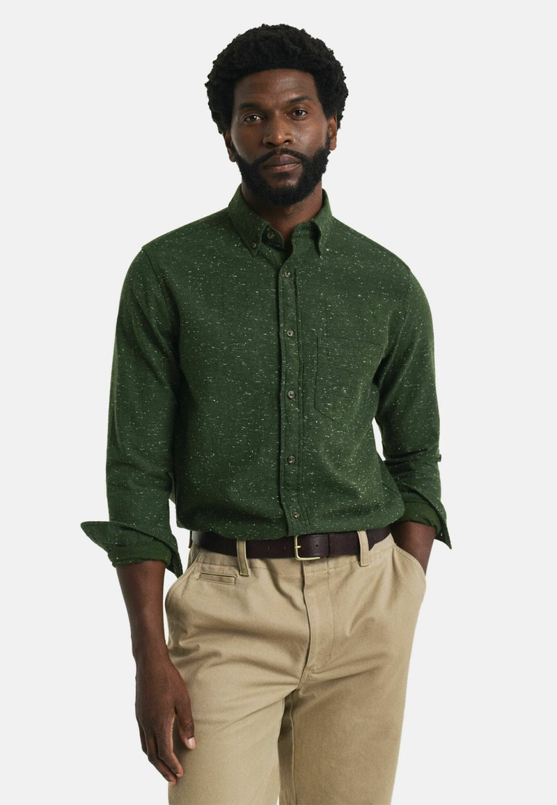 Groen gespikkelde overhemdd met lange mouwen, borstzak en een brede kraag, gecombineerd met lichtbeige broeken en een bruine riem.