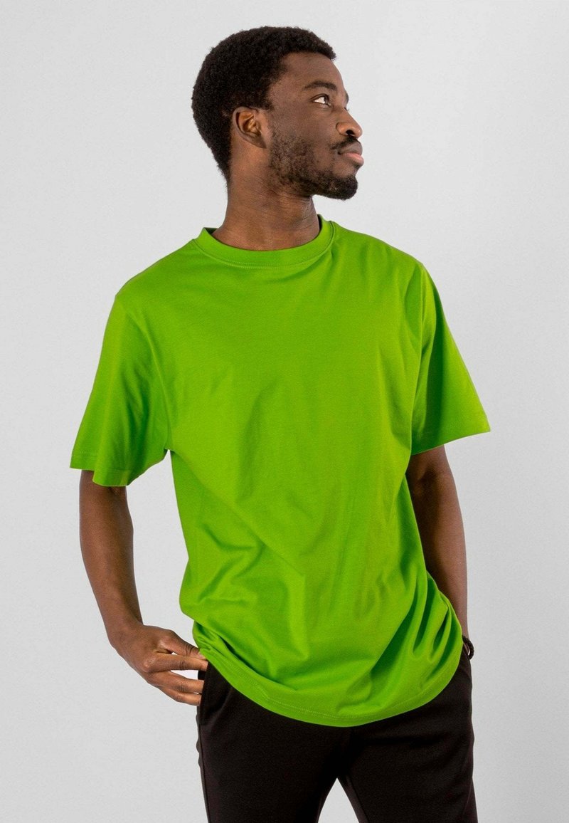 Lys grøn bomulds t-shirt med korte ærmer, rund halsudskæring og en afslappet pasform. Kombineret med sorte bukser. Neutral baggrund.