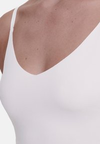 White tank top featuring a deep V-neckline, thin straps, and a fitted design, made from smooth, stretchy fabric with a matte finish.
